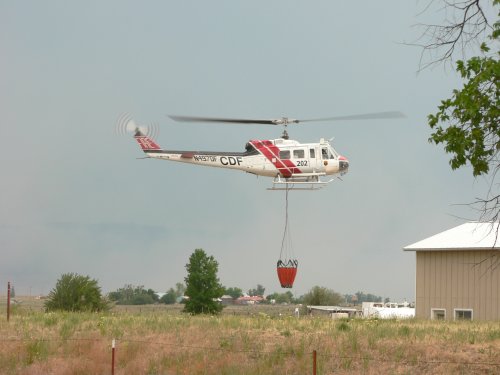A white and red CDF helicopter taking off with a suspended water bag.
